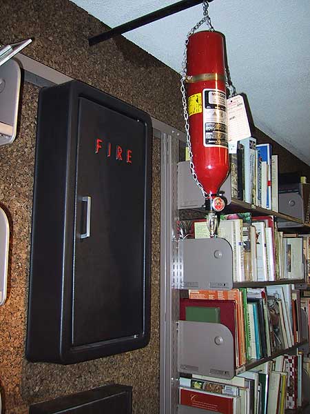 [I had to see this set-up twice before I understood what it was -- it was a standalone fire extinguisher type thing suspended from the ceiling over what appeared to be a metal seat coming out from the wall. The metal seat turned out to be a book drop [minus the cart for the books to drop into it's really difficult to identify] and the fire extinguisher is actually a sprinkler system for the [non-present] books in the bookdrop cart.
]